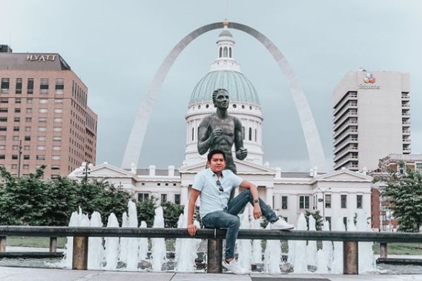 A man sits on a ledge with the Old Courthouse and Gateway Arch in the background