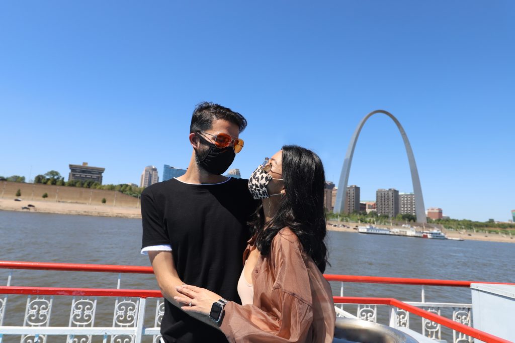 Asian couple standing on the upper deck of the Riverboat with the Arch in the background