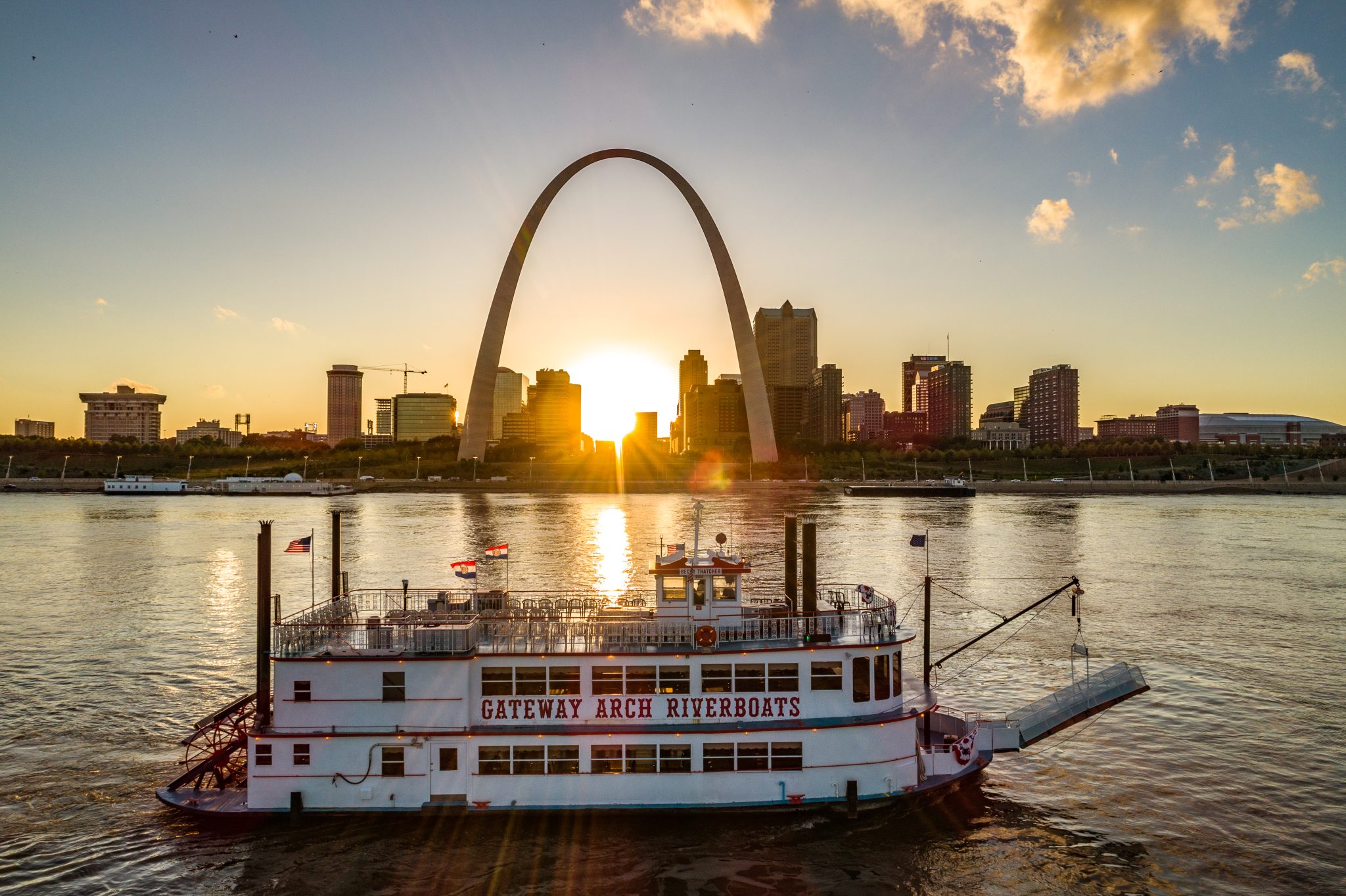 The Becky Thatcher riverboat floats past the Gateway Arch during sunset.