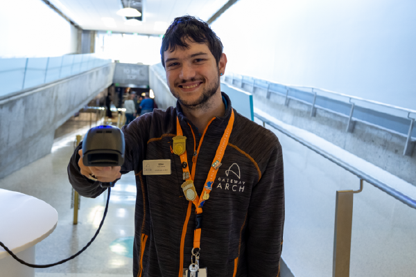 Gateway Arch Tour Guides is smiling at the Tram Lobby and reaches out with a ticket scanner.