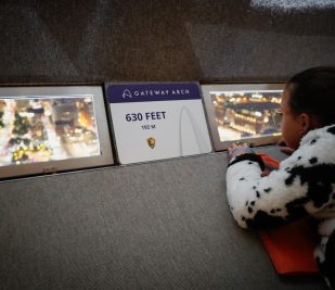 A young girl dressed in a Halloween costume looks out a window at the top of the Gateway Arch.