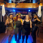 Four female guests are in Halloween costumes and pose for a photo on the Halloween Costume Party Cruise on the Riverboat.