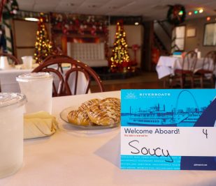 A placemat is set on a table with drinks, silverware and cinnamon rolls before a cruise on the Riverboats at the Gateway Arch.