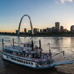 The Becky Thatcher riverboat floats past the Gateway Arch during sunset.