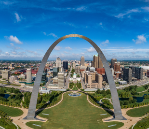 Aerial image of Gateway Arch National Park looking west into downtown St. Louis on a sunny day with a bright blue sky.