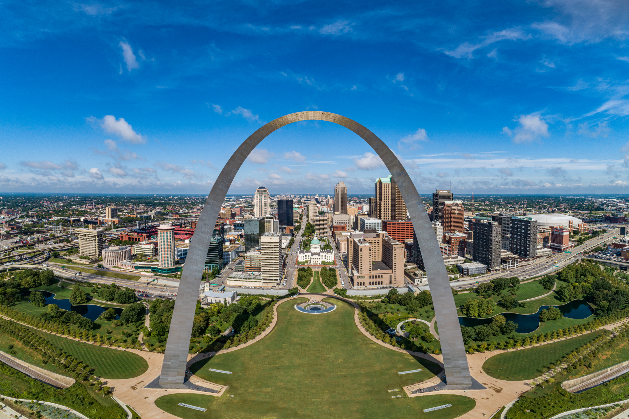 Aerial image of Gateway Arch National Park looking west into downtown St. Louis on a sunny day with a bright blue sky.