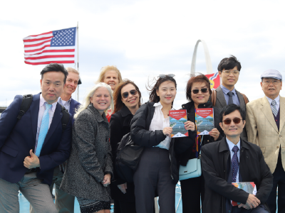 A group of visitors dressed in business attire pose for a photo in front of the Gateway Arch on the top deck of a cruise at the Riverboats at the Gateway Arch.