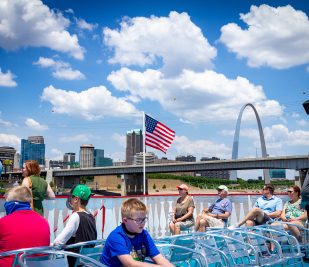 Guests on the top deck of the Tom Sawyer riverboat soak in the beautiful views of St. Louis with the Gateway Arch in the background.
