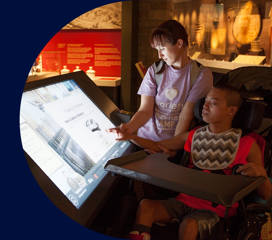 Child in a motorized wheelchair and a friend playing with interactive elements in the museum.