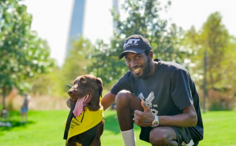 A man showing a thumbs up while crouching down next to his dog wearing a BARK ranger bandana.