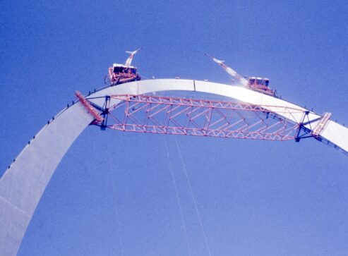Historic image of the Gateway Arch construction where the last piece is inserted into the top. Two cranes are on top of the arch to complete the project.