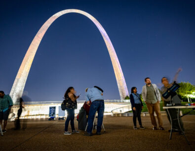 Gateway Arch National Park visitors look through a telescope at night during a Gateway to the Stars event
