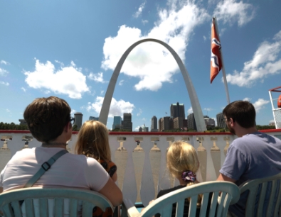 Family sitting on the top deck of the riverboat and looking at the St. Louis skyline.