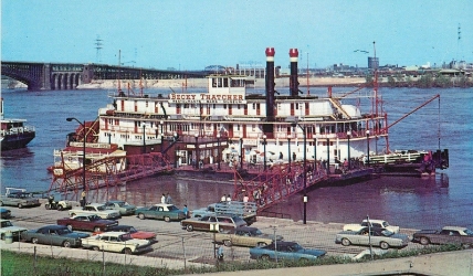 People entering a ramp on a dock that has multiple structures on it. This dock sits in front of a large riverboat named "Becky Thatcher."
