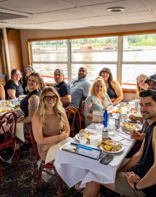 Two tables of friends enjoying a Brunch Cruise on the Riverboats with plates full of food in front of them