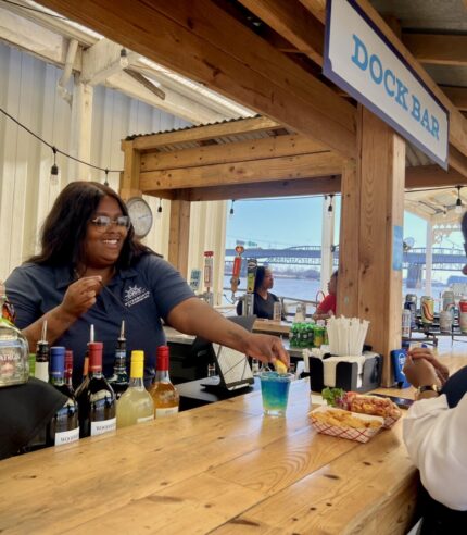 Bartender on the Riverboats Dock Bar makes a drink and serves food to a customer sitting at the bar