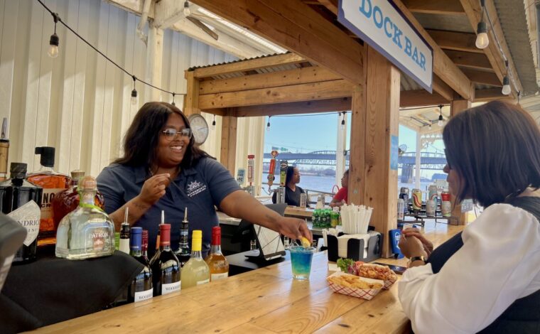 Bartender on the Riverboats Dock Bar makes a drink and serves food to a customer sitting at the bar