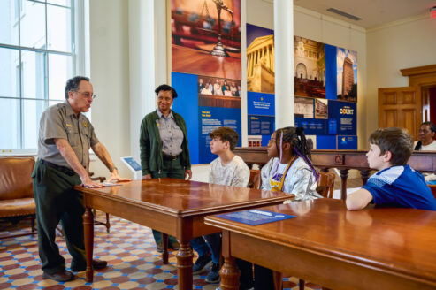 A pair of Gateway Arch National Park rangers speak to student seated inside a mock courtroom in the Old Courthouse