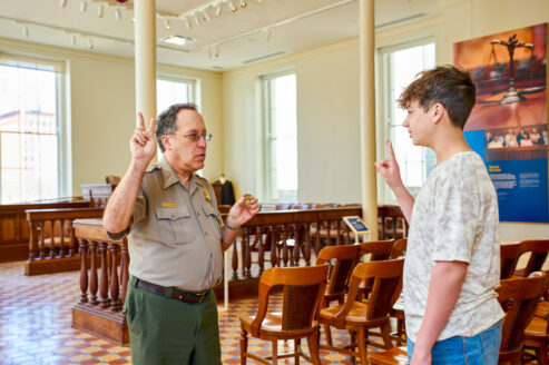 A Gateway Arch National Park ranger swears in a young visitor as a Jr. Ranger inside a courtroom in the Old Courthouse