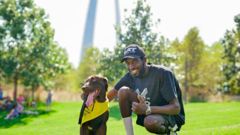 Gateway Arch visitor poses with his chocolate lab dog, wearing a B.A.R.K. Ranger bandana at Gateway Arch National Park