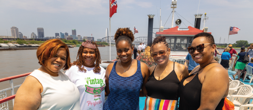 A group of women pose for a photo on the top deck of the riverboat on a sunny, warm day