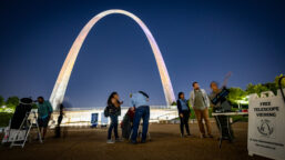 People look into telescopes in front of the Gateway Arch at night during a Gateway to the Stars event