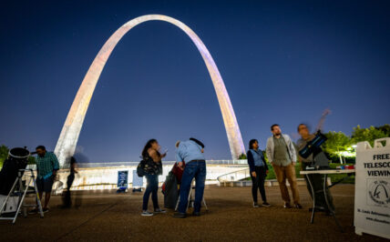 People look into telescopes in front of the Gateway Arch at night during a Gateway to the Stars event