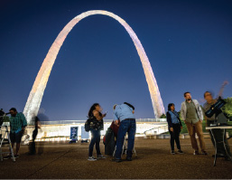 People look into telescopes in front of the Gateway Arch at night during a Gateway to the Stars event
