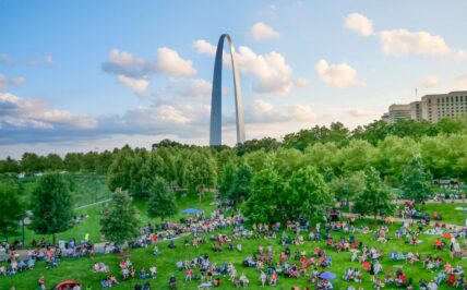 View of Gateway Arch National Park with hundreds of people sitting and watching a blues concert during Blues at the Arch Festival.