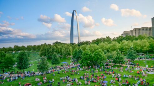 View of Gateway Arch National Park with hundreds of people sitting and watching a blues concert during Blues at the Arch Festival.