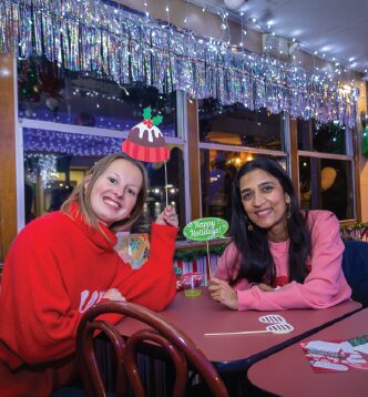 Two women dressed in holiday attire on The Floating Sleigh Holiday pop-up bar.
