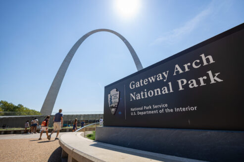 Visitors walking into the visitor center entrance at Gateway Arch National Park on a sunny summer day.