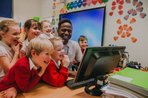 Teacher and group of students at a computer together.
